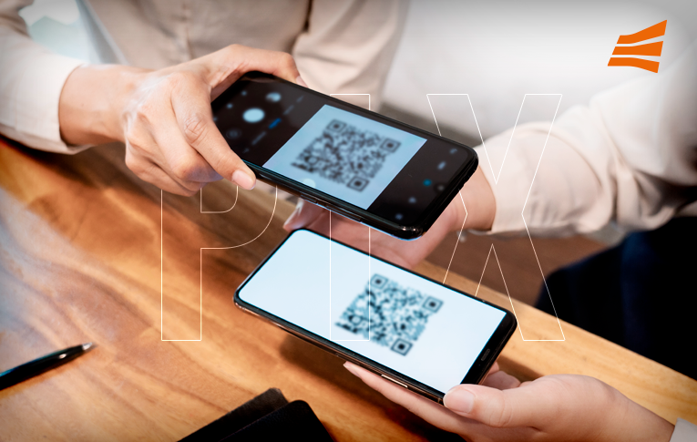 Na imagem: dois celulares sobre a mesa, um deles mostra o QR Code, enquanto o segundo faz a leitura do código para realizar o pagamento instantâneo PIX