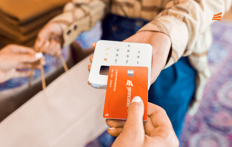 Uma mão segurando o cartão contactless Gerencianet próximo a uma maquininha para realizar o pagamento por aproximação. Na outra mão, a sacola de compra sendo entregue para a cliente.