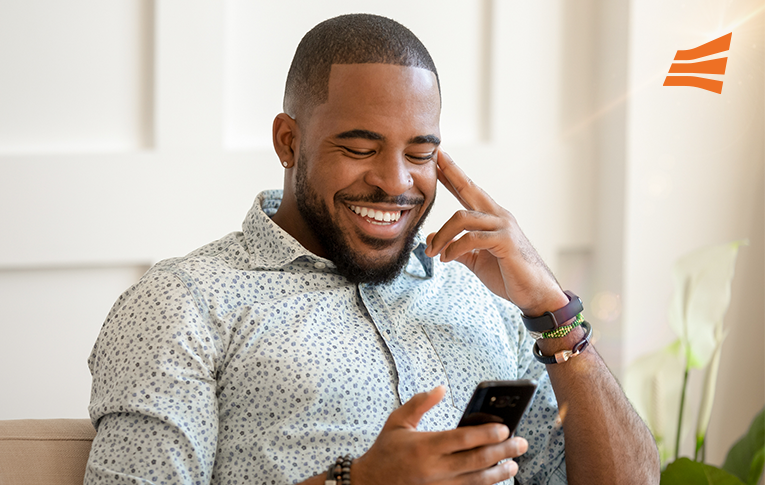 Na imagem: homem negro sorrindo enquanto olha para o smartphone, que está em sua mão direita, simbolizando a tranquilidade e segurança em utilizar a assinatura eletrônica.