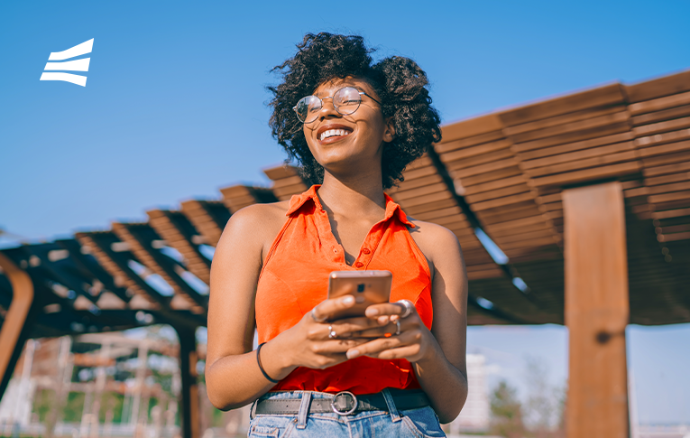 Mulher negra sorrindo com um smartphone nas mãos pesquisando como pagar com Pix.