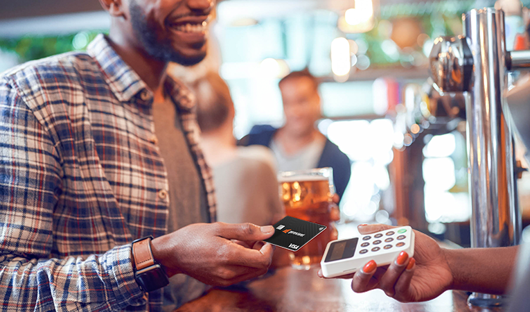 Homem sorrindo enquanto entrega seu cartão pré-pago da Conta Digital da Gerencianet para realizar o pagamento pelo consumo em uma chopperia.