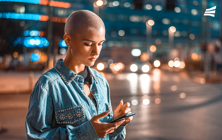 Mulher em uma avenida movimentada à noite com um smartphone nas mãos lendo sobre as novas regras do Pix