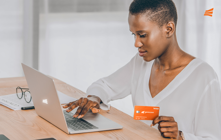 Mulher negra, empresária, sentada em uma mesa de escritório com um Cartão de Crédito PJ nas mãos